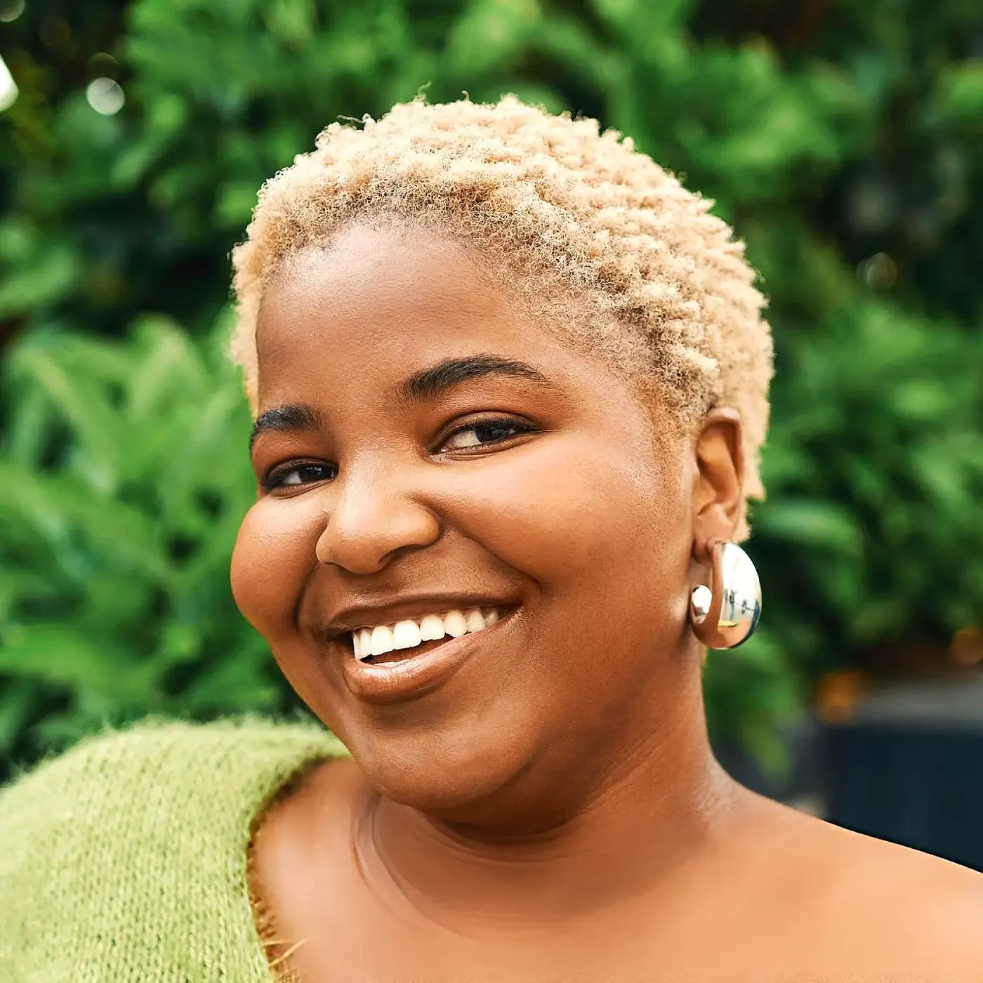 Adeola, smiling outdoors in a green knitted top